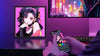 Divoom Pixoo-64 pixel display on a purple-lit desk showing pixel art while a hand controls it from the Divoom app on a smartphone