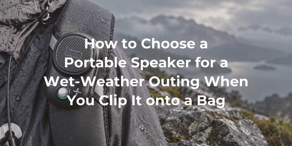 A clip-on speaker on a gray bag in a sheltered outdoor setting.