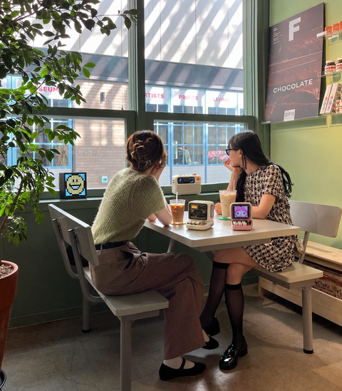 Two friends talking in a cafe with Divoom displays on the table